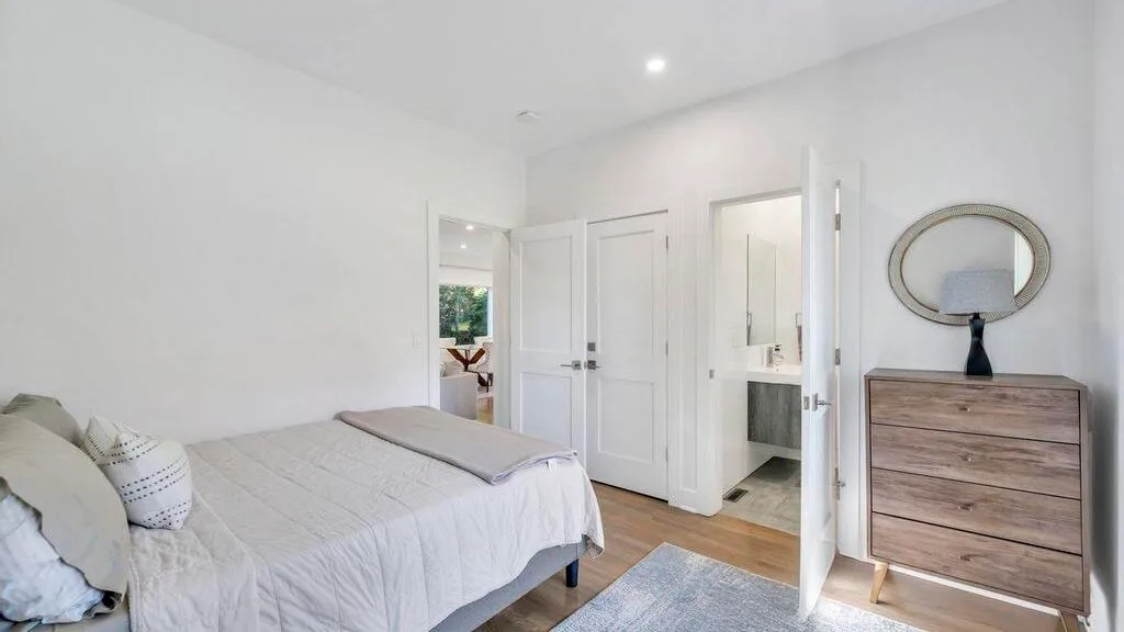 Un dormitorio luminoso con una cama y una cómoda de madera junto a la puerta.
