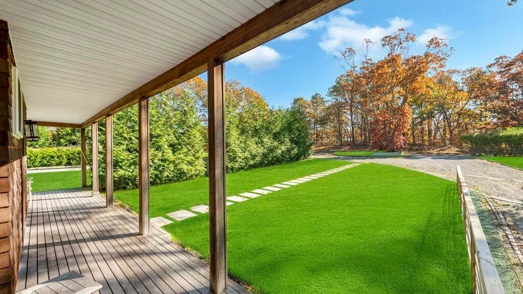 Una terraza de madera cubierta da a un césped verde y un jardín.