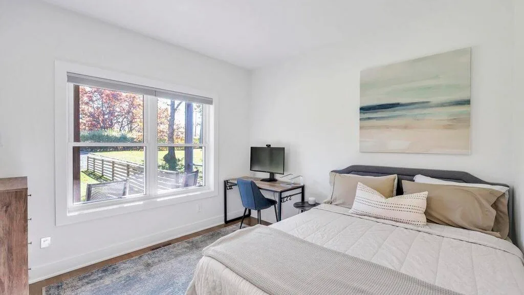 Un dormitorio luminoso con una cama tendida y una ventana amplia.