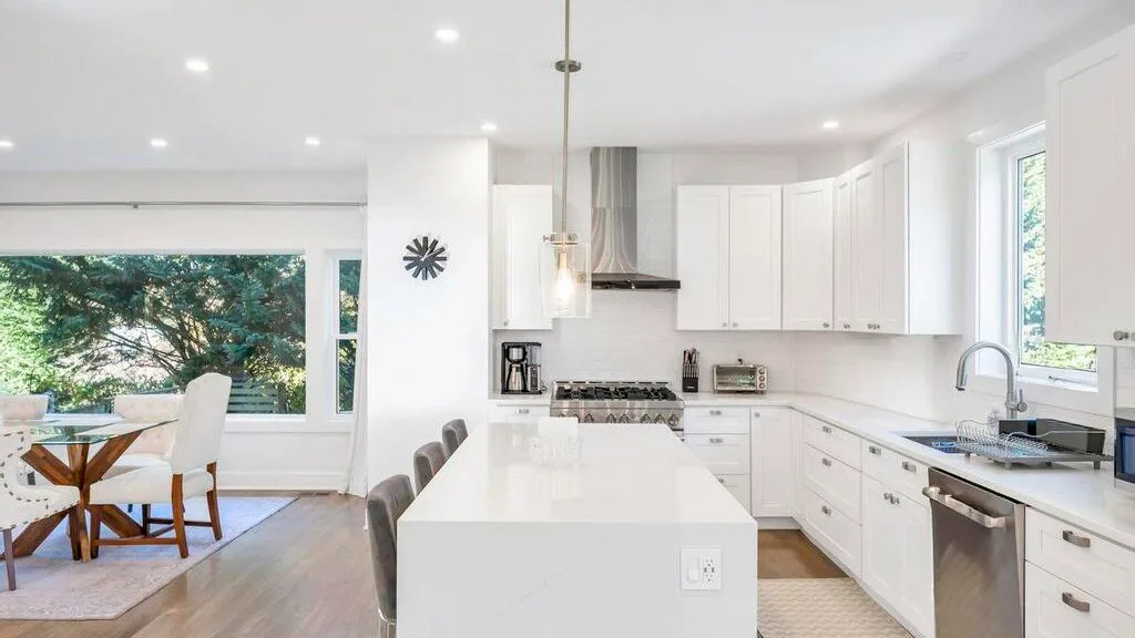 Una cocina blanca y luminosa con una isla central y un comedor junto a las ventanas.