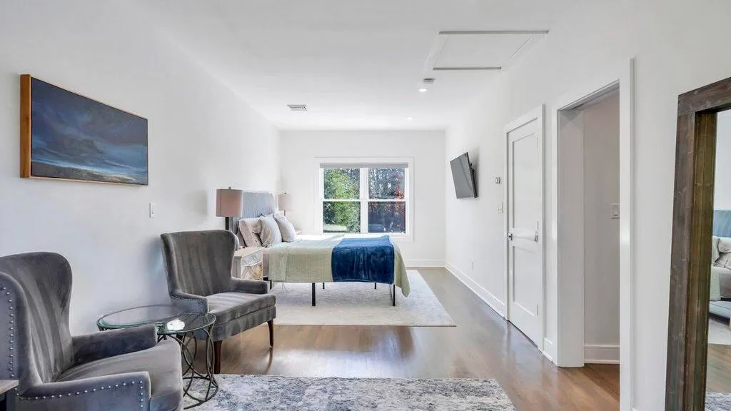 Un dormitorio luminoso con una cama, una ventana y asientos junto a la pared.