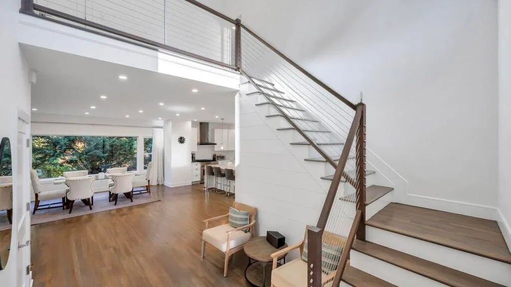 Un espacio abierto de sala y comedor con una escalera y ventanas grandes.