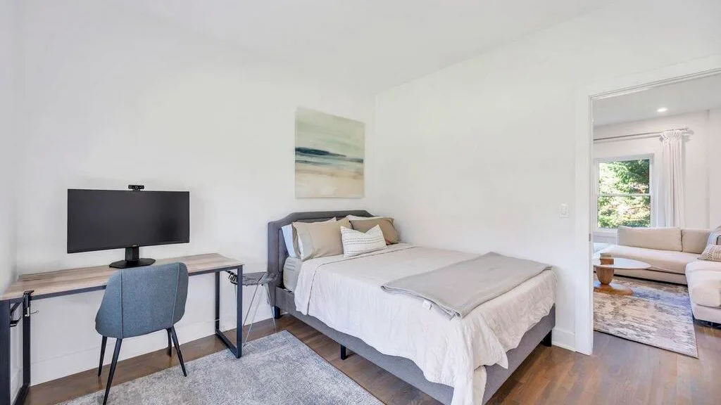 Un dormitorio luminoso con una cama arreglada y un escritorio junto a la pared.