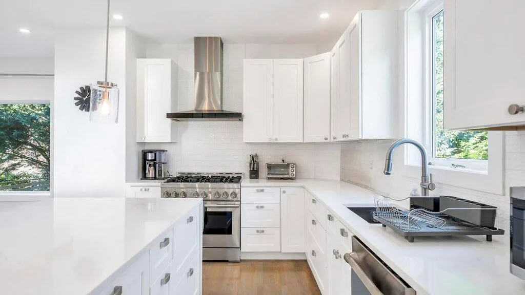 Una cocina blanca y luminosa con isla, gabinetes y una ventana grande.