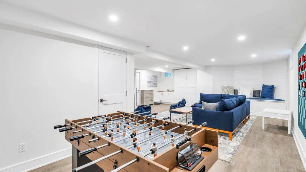 Una luminosa sala de recreación en el sótano, con futbolín y asientos azules.