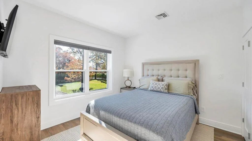 Un dormitorio luminoso con una cama junto a una ventana grande que da a zonas verdes.
