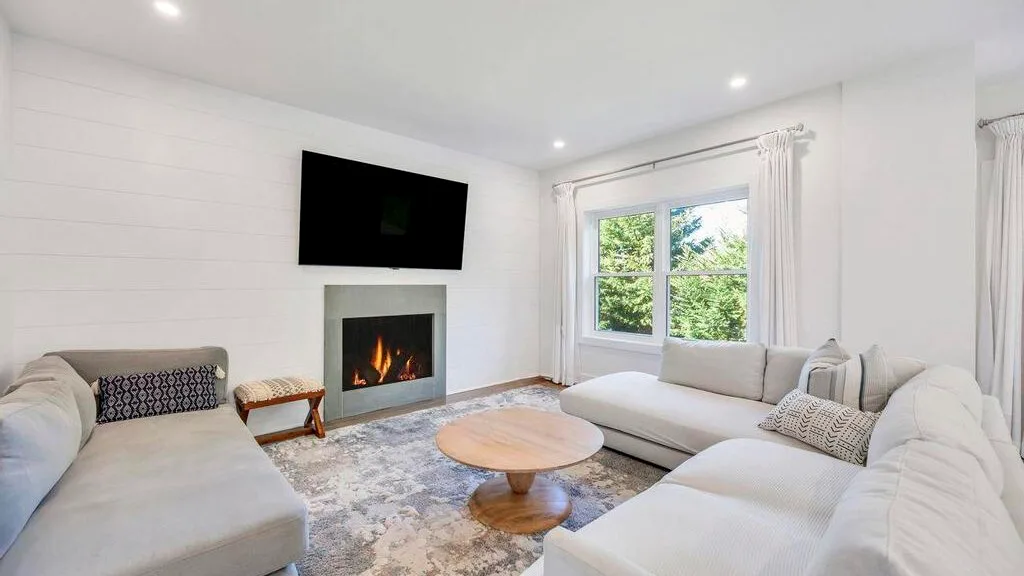 Una sala luminosa con asientos claros, una chimenea y un televisor montado en la pared.