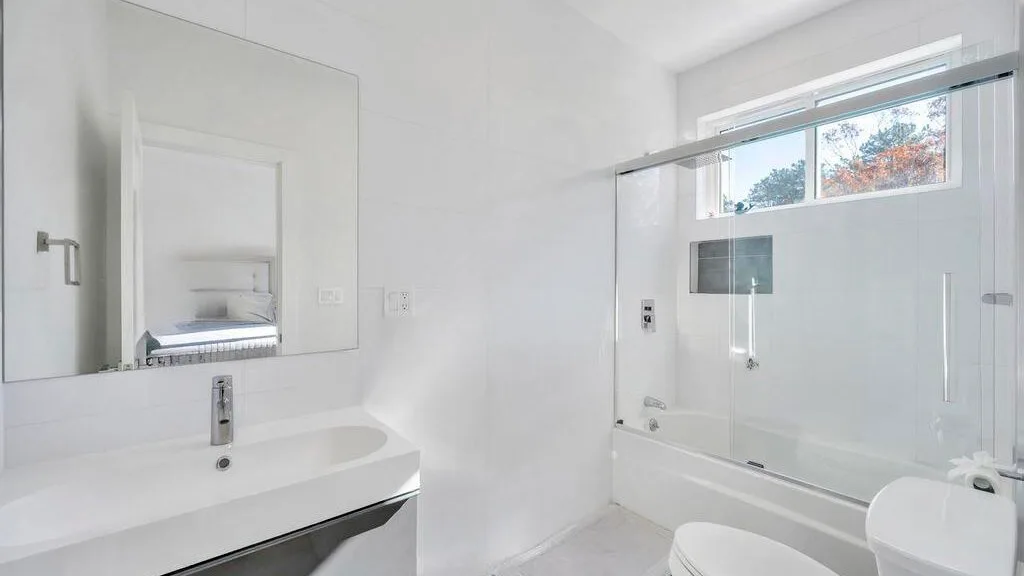 Un baño luminoso con lavabo, espejo y bañera bajo una ventana.