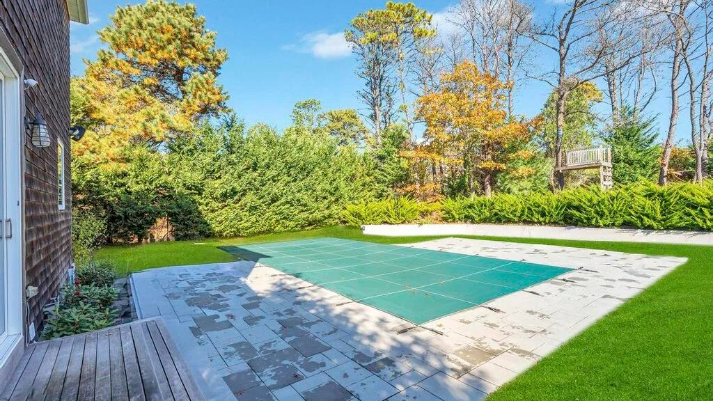 Una piscina exterior cubierta junto a un patio pavimentado y césped verde.