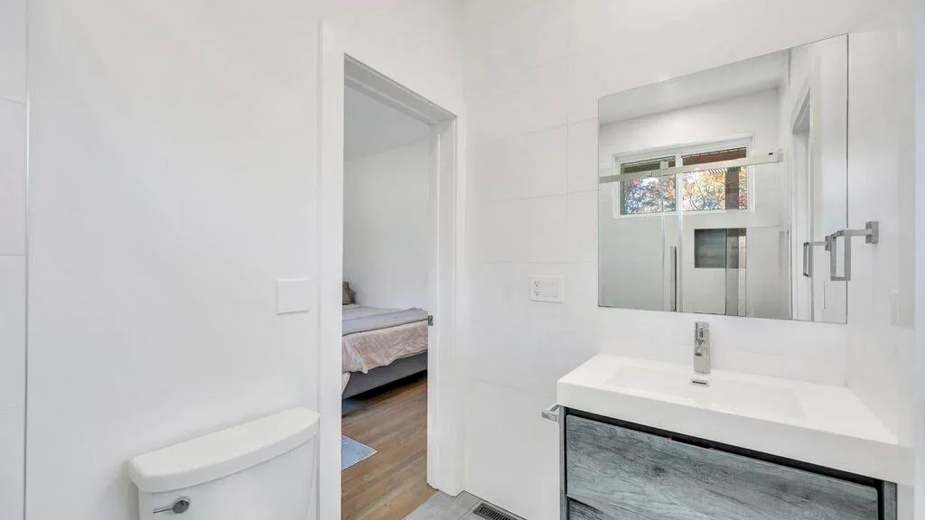 Un baño luminoso con lavabo y espejo junto a una puerta abierta.