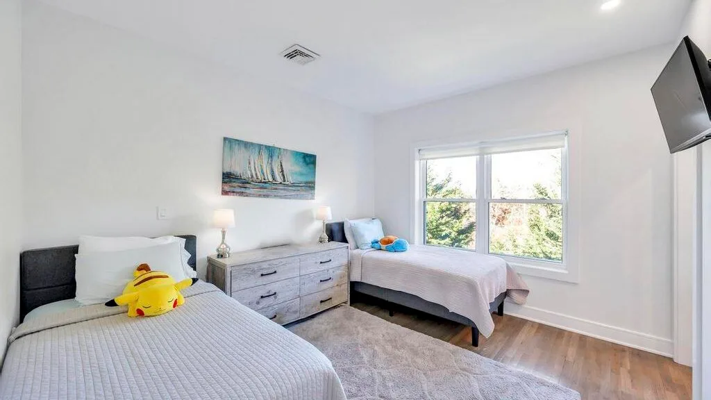 Un dormitorio luminoso con dos camas, una cómoda y una ventana grande.
