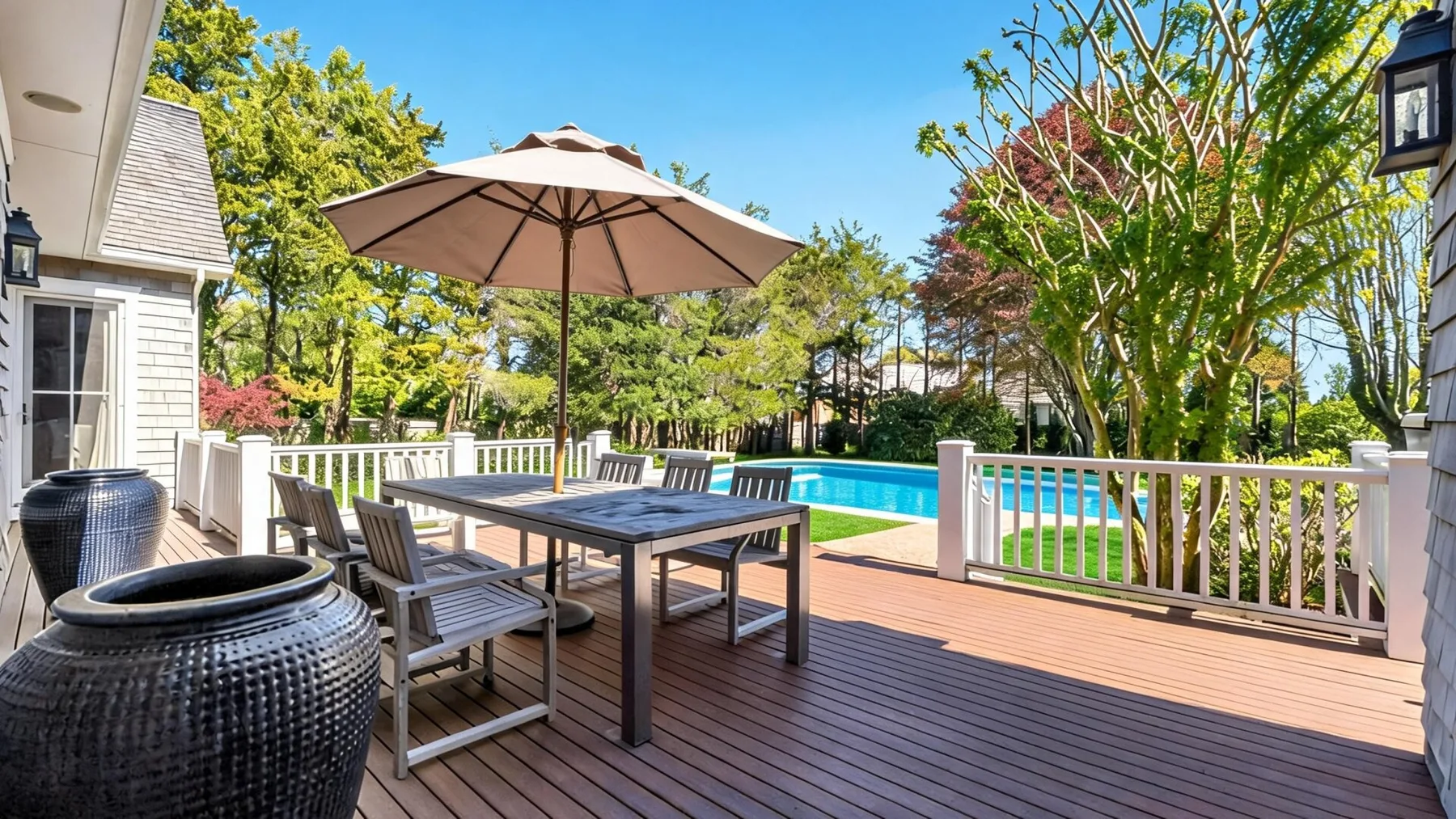 A wooden deck beside a swimming pool has outdoor seating under a large umbrella.