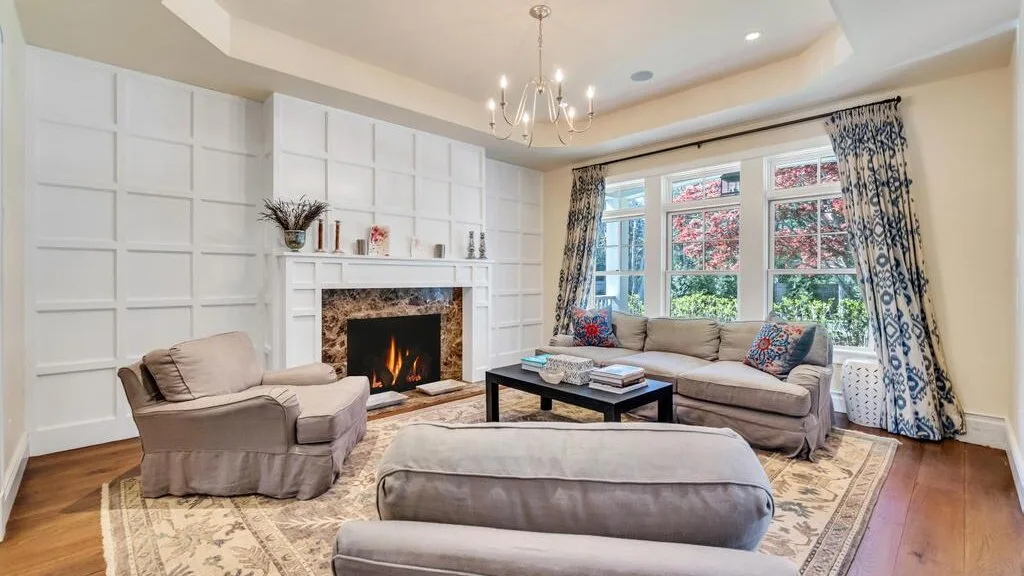 A living room with seating arranged around a fireplace and large windows.