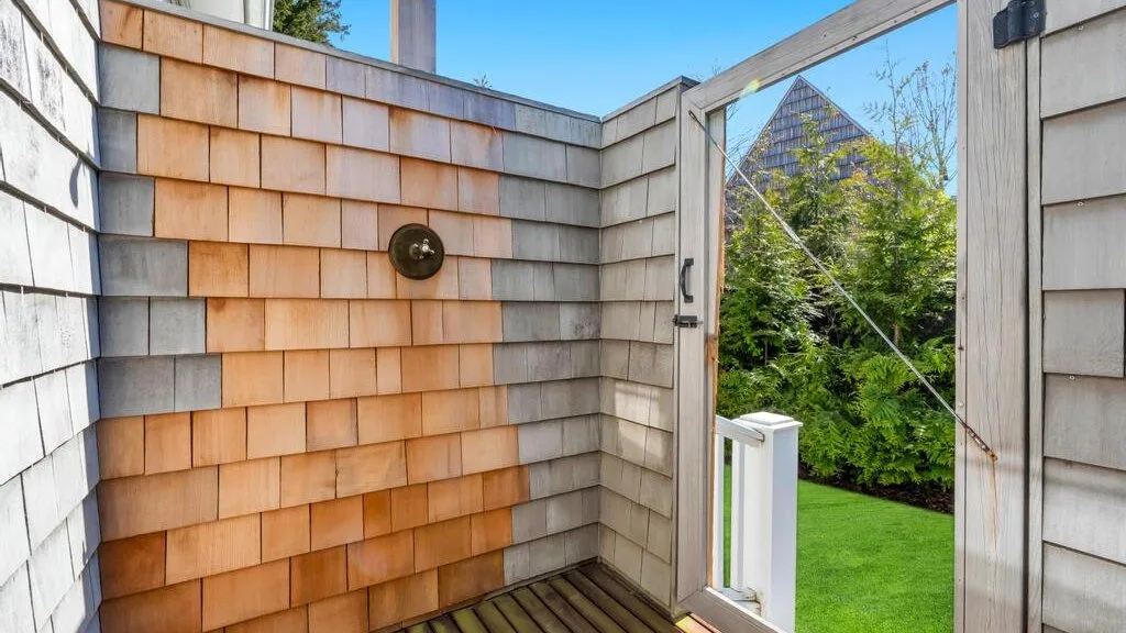 An outdoor shower area opens through a wooden gate to a green garden.
