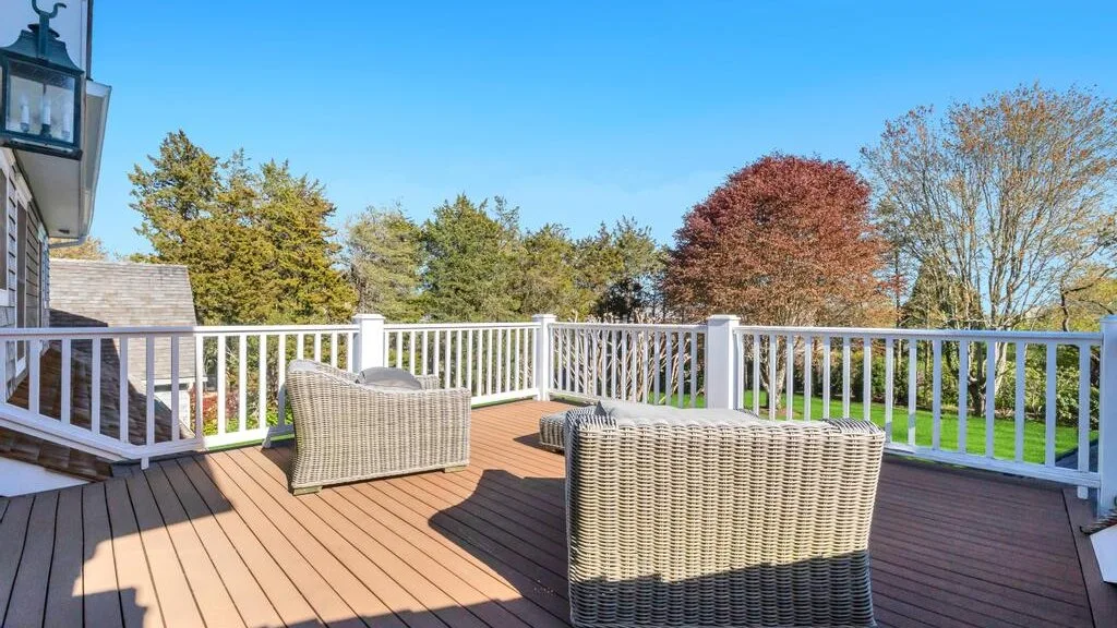 An outdoor deck with woven seating overlooks a green lawn and trees.