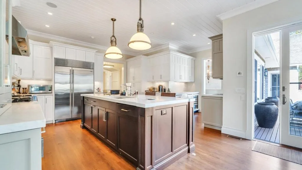 A bright kitchen with a large island, white cabinets, and stainless steel appliances.
