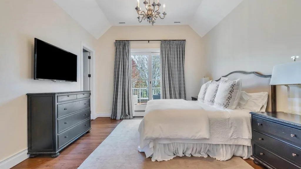 A bright bedroom with a made bed and curtained glass doors.