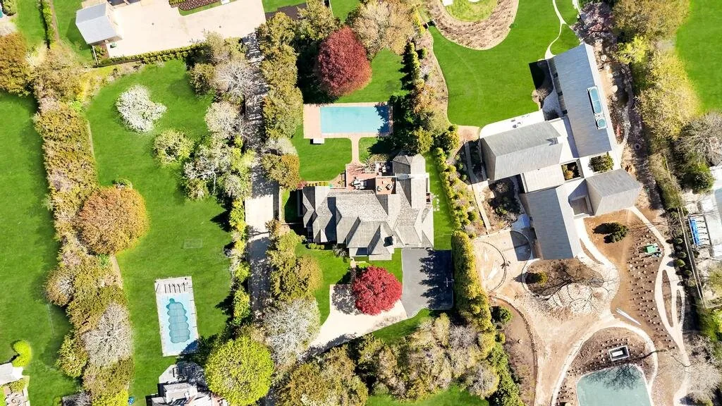 An aerial view of a landscaped property with a central house, lawns, and a swimming pool.