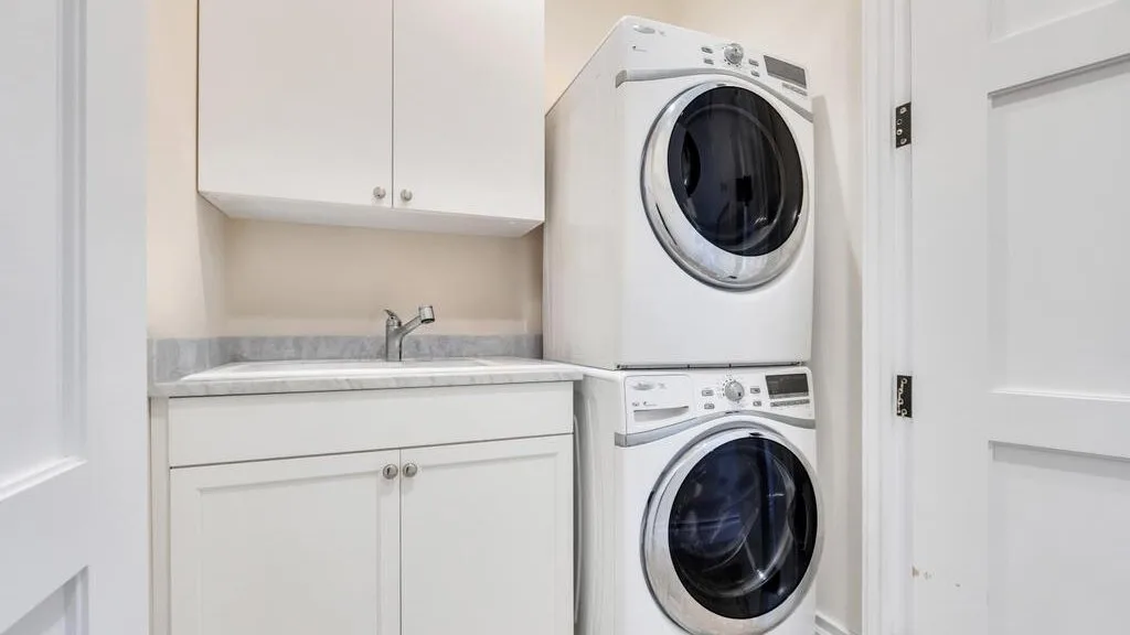 A laundry room with stacked front-loading machines beside a sink and cabinets.