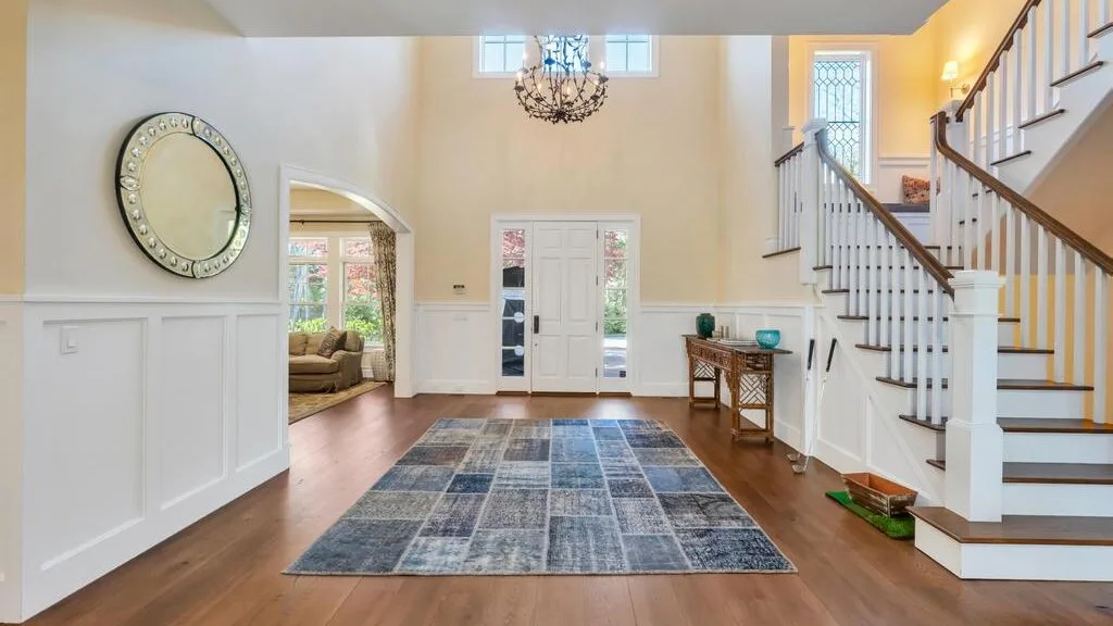 A bright foyer features a staircase and a patterned rug on the wood floor.