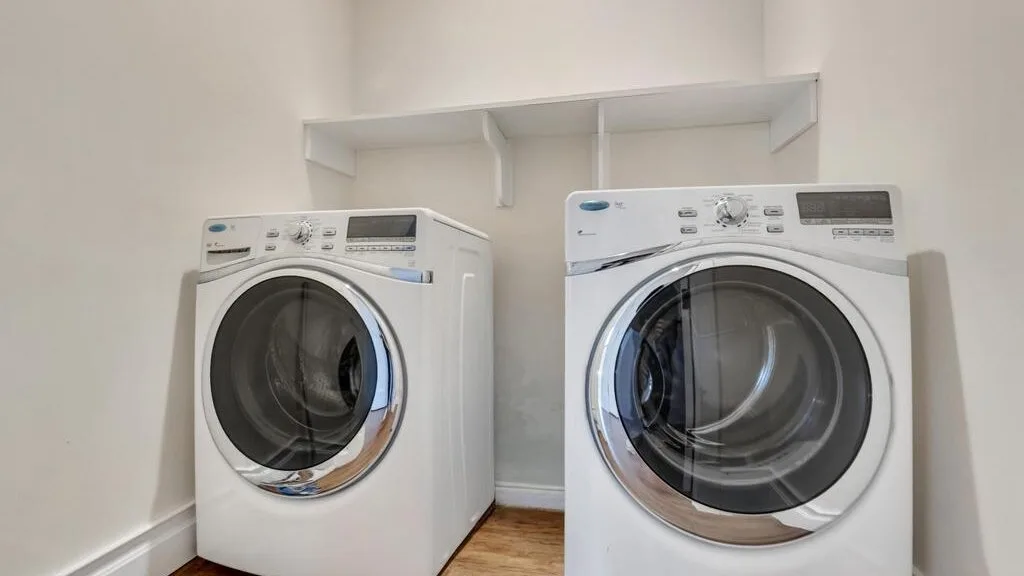 A laundry area with two front-loading washing machines beneath a wall shelf.