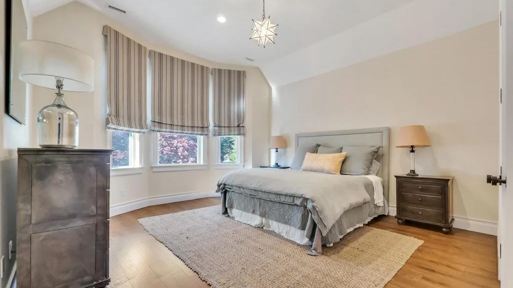 A bedroom with a bed, bedside tables, and windows with striped curtains.