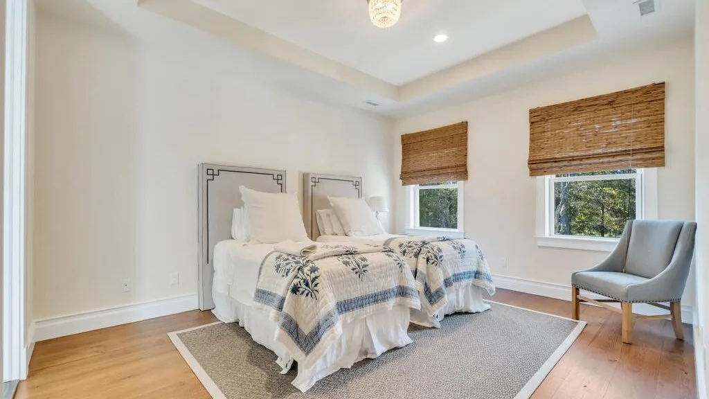 A bright bedroom with two beds and a gray rug.