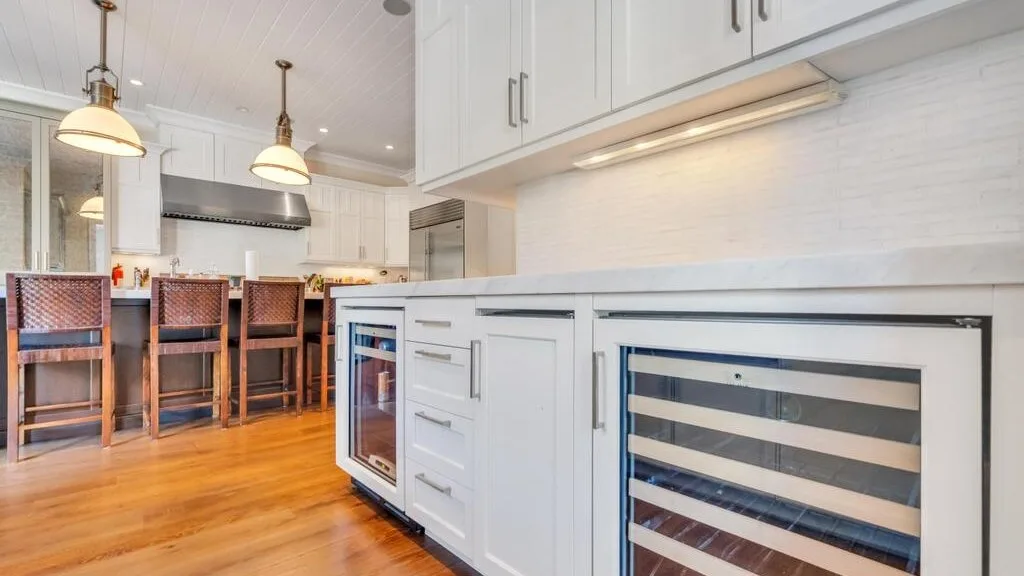 A bright kitchen with white cabinets, a long counter, and bar seating.