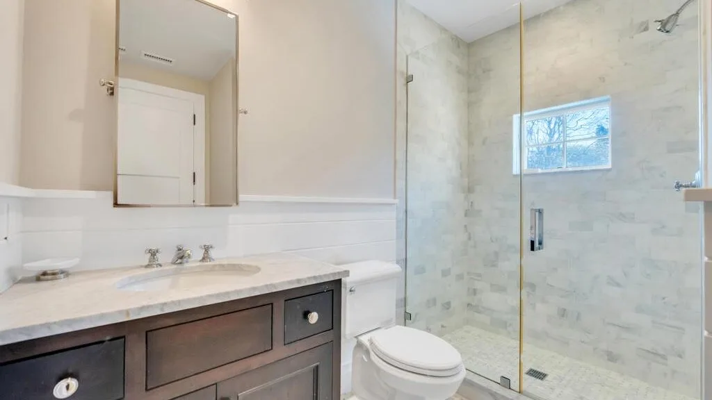 A bathroom vanity with a sink sits beside a glass shower and toilet.
