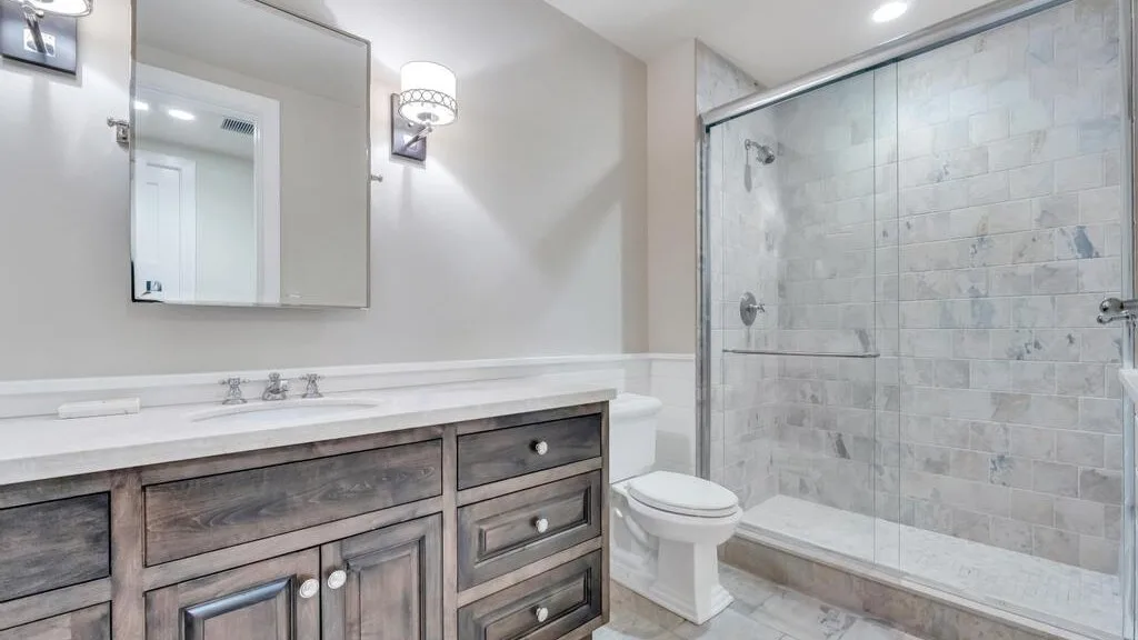 A bright bathroom with a long vanity and a glass-enclosed shower.