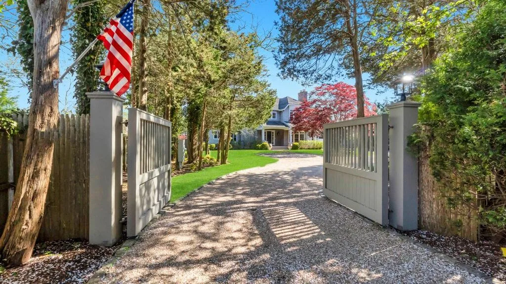A tree-lined gravel driveway passes through open gates toward a house.
