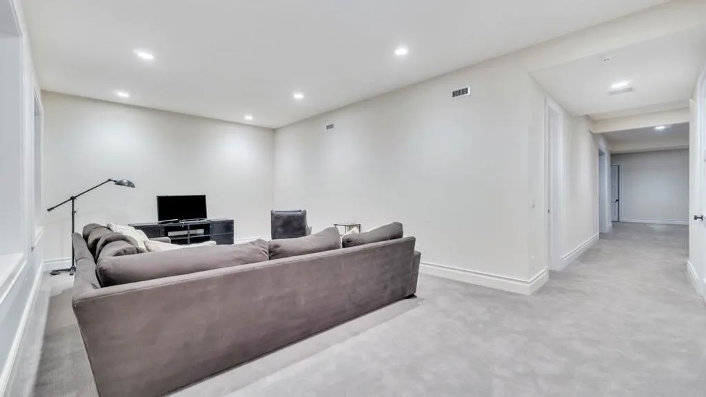 A living room with gray seating, a television, and a hallway opening.