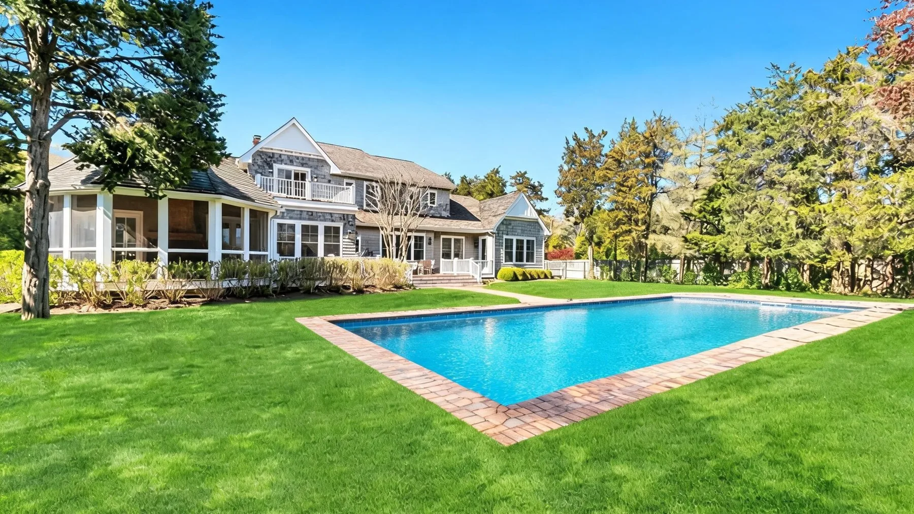 A large house overlooks a rectangular swimming pool set in a green lawn.