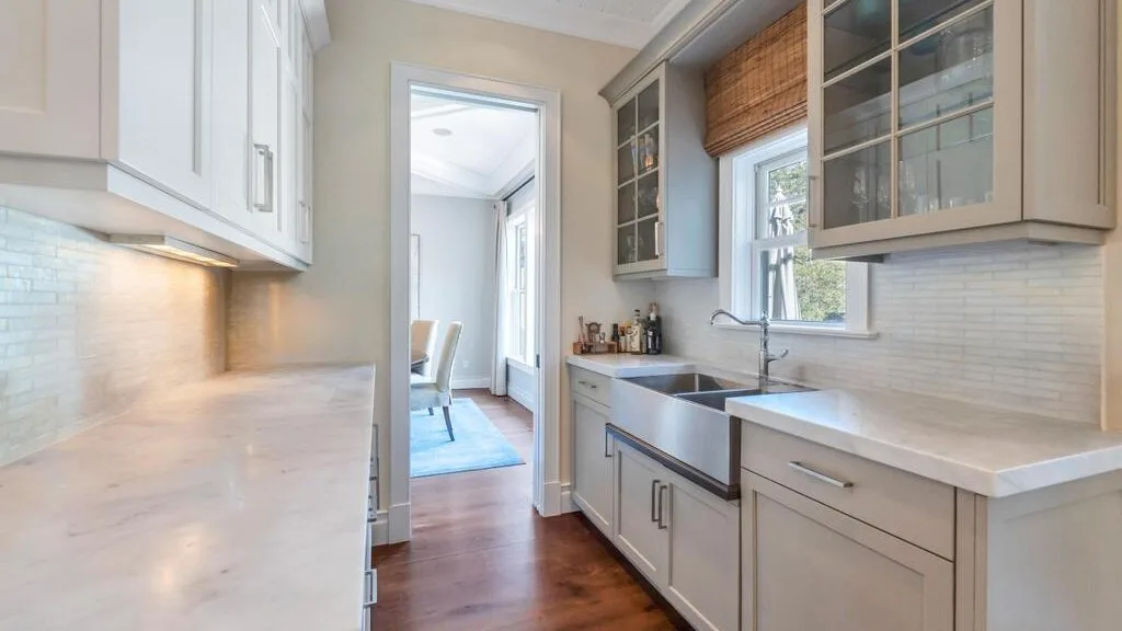 A bright kitchen with white cabinets, a sink, and a central work surface.