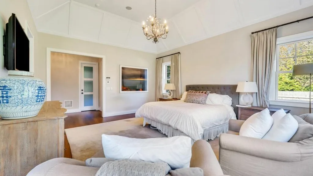 A bright bedroom with a large bed, a sitting area, and a chandelier.