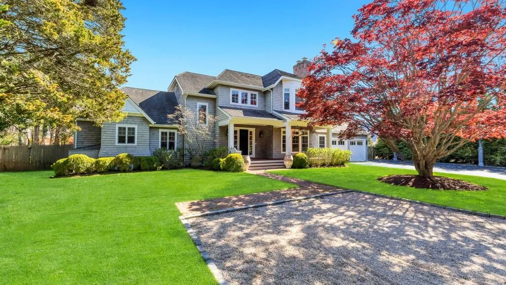 A large house stands beyond a green lawn and a paved driveway.