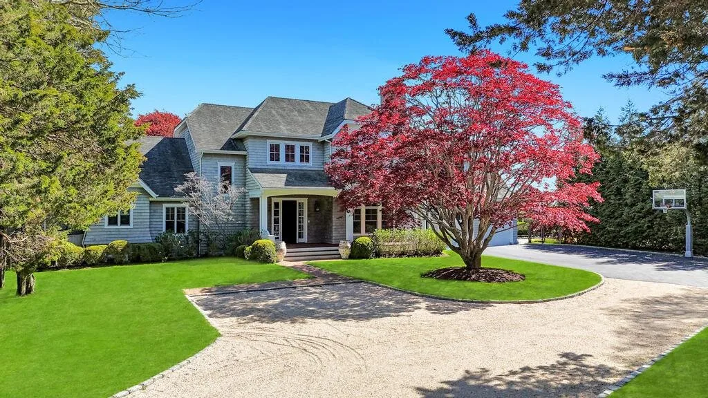 A large house stands beside a curved driveway and a red-leaved tree.