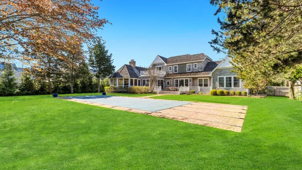 A large house stands beyond a broad green lawn and paved patio.