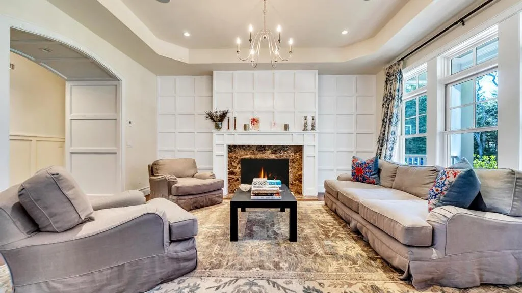 A living room with upholstered seating, a fireplace, and large windows.