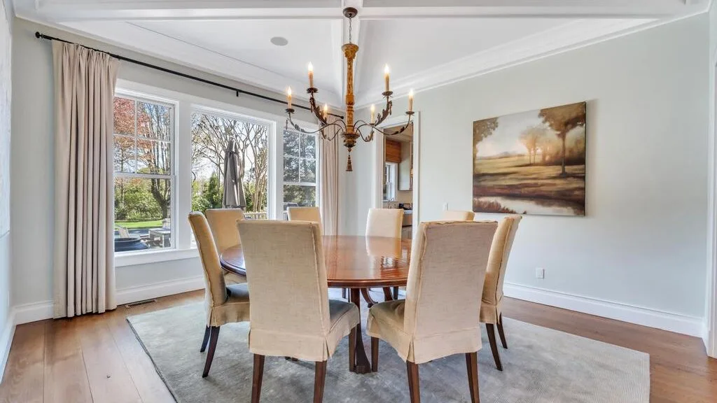 A dining room with a wooden table, upholstered seating, and large windows.