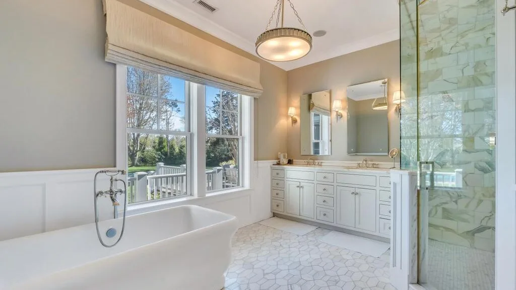 A bright bathroom with a bathtub, vanity, and large windows.