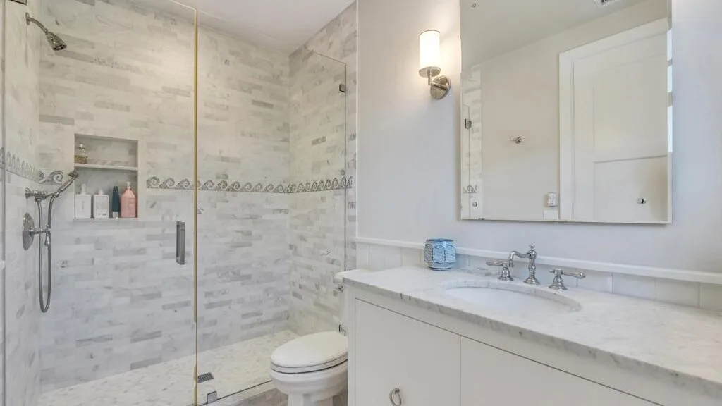 A bright bathroom with a glass shower, toilet, and vanity.