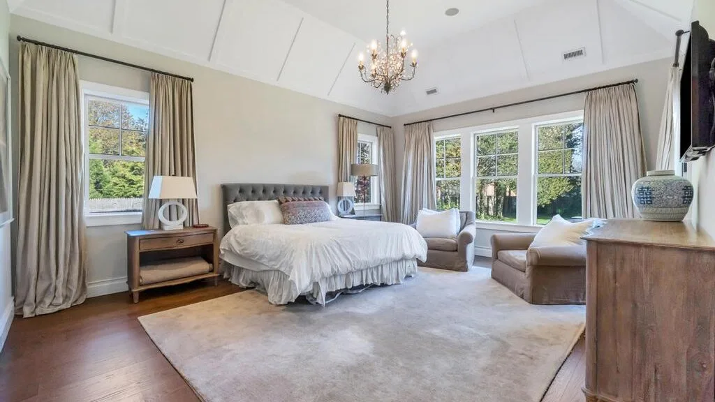 A bright bedroom with a bed and large windows overlooking greenery.