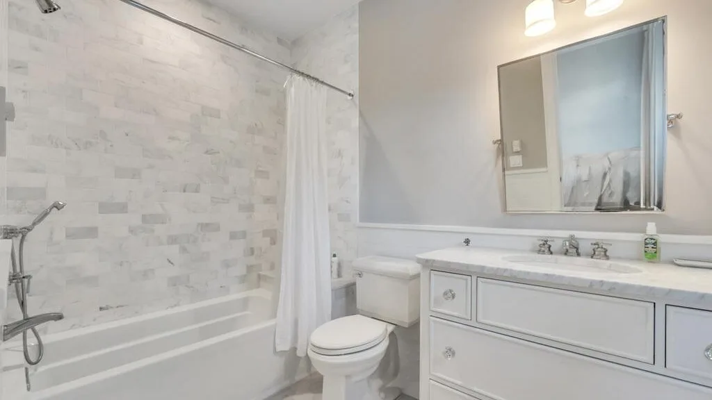 A bathroom with a bathtub, shower curtain, toilet, and sink.