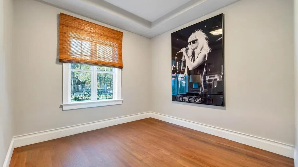An empty room with wood flooring, a window, and a large framed portrait.