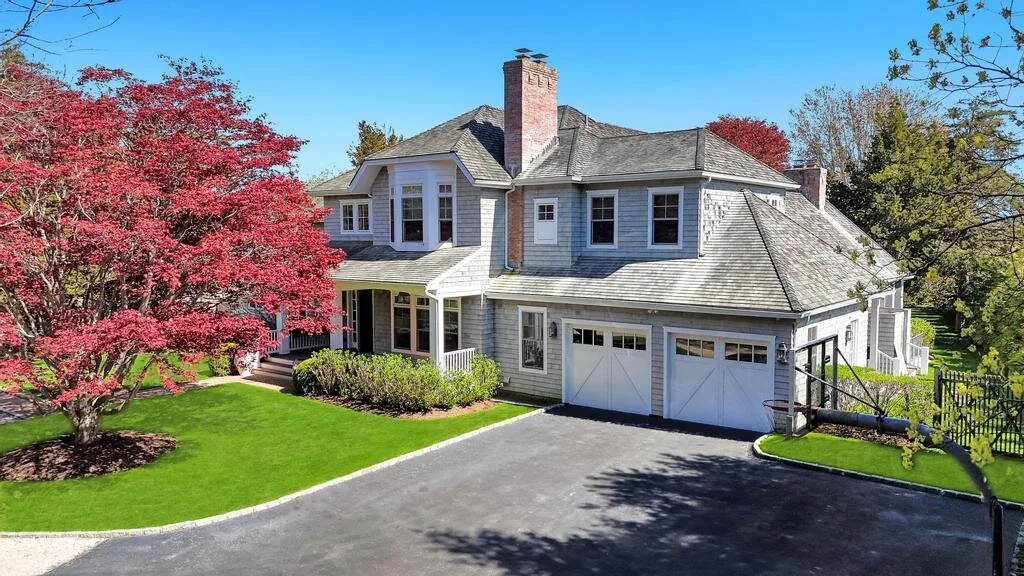 A large house with gray siding, white garage doors, and a green lawn.