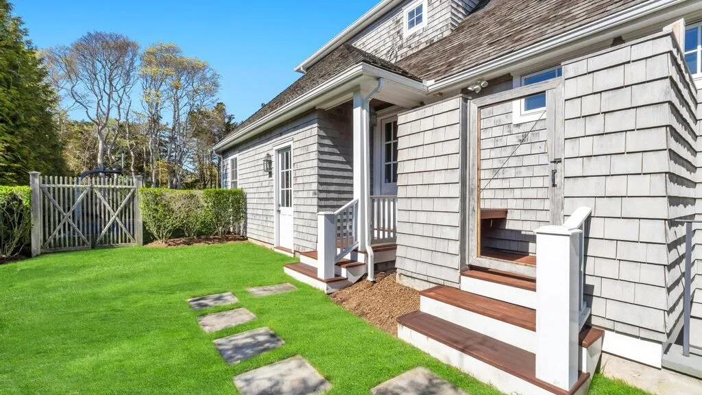 A shingled house with white steps opens onto a green lawn.