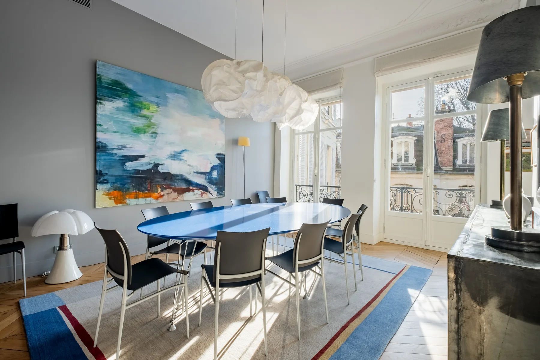 A bright dining area has a long table beneath sculptural pendant lights.
