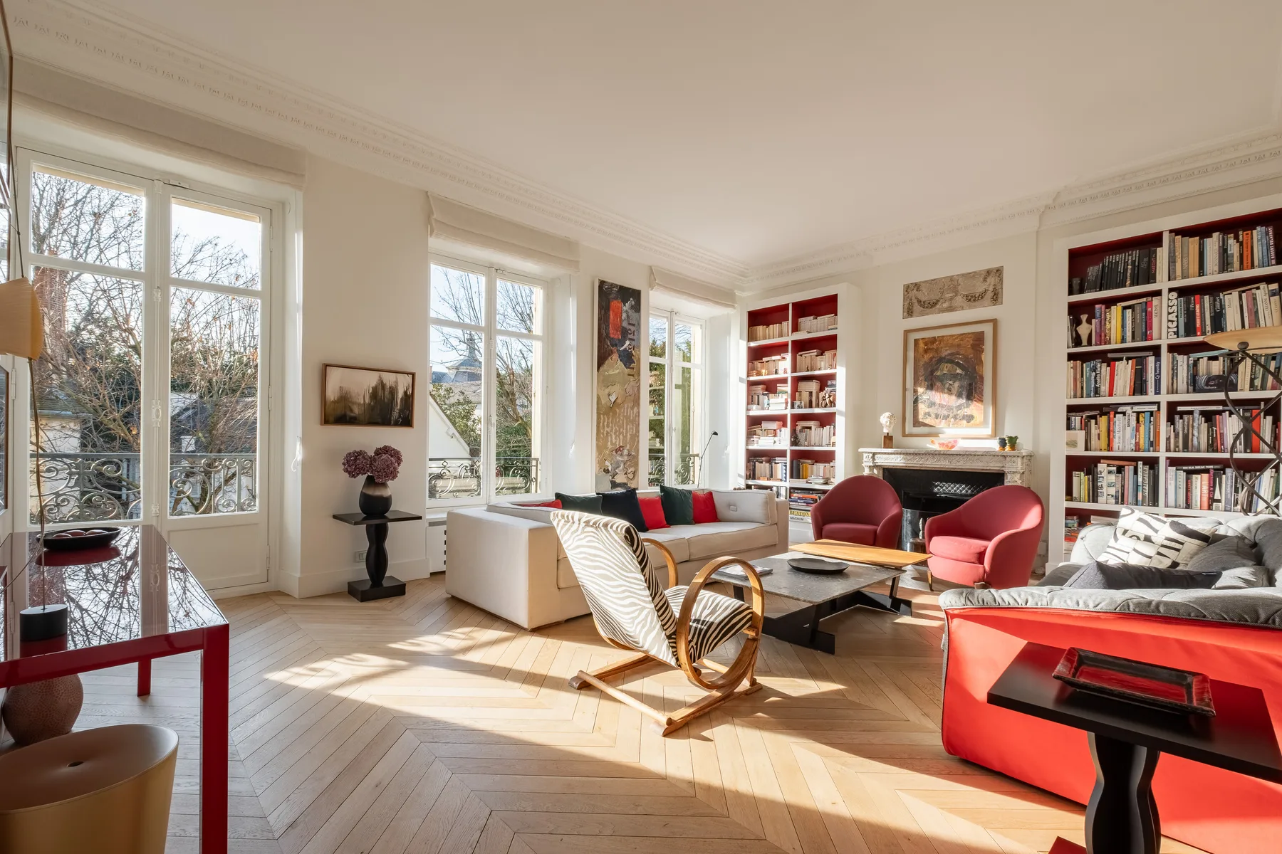 A bright living room with bookshelves, seating, and tall windows.