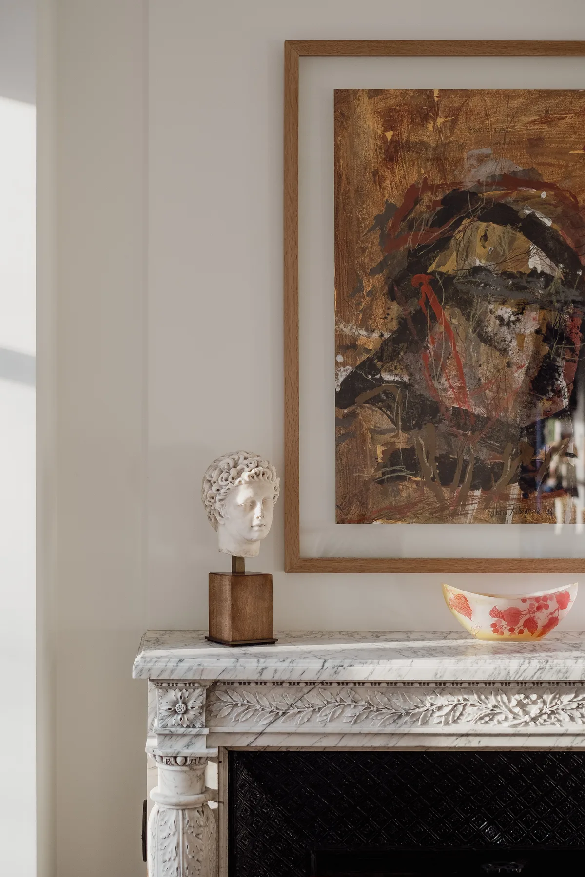A bright interior features a carved fireplace beneath a framed abstract painting.